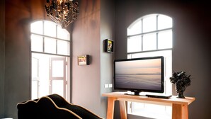 Una camera moderna con un'ampia finestra, una TV a schermo piatto su un supporto in legno, un divano nero e una pianta decorativa.