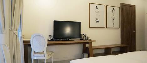 A hotel room with a bed, a desk with a computer, a chair, and two framed pictures on the wall.