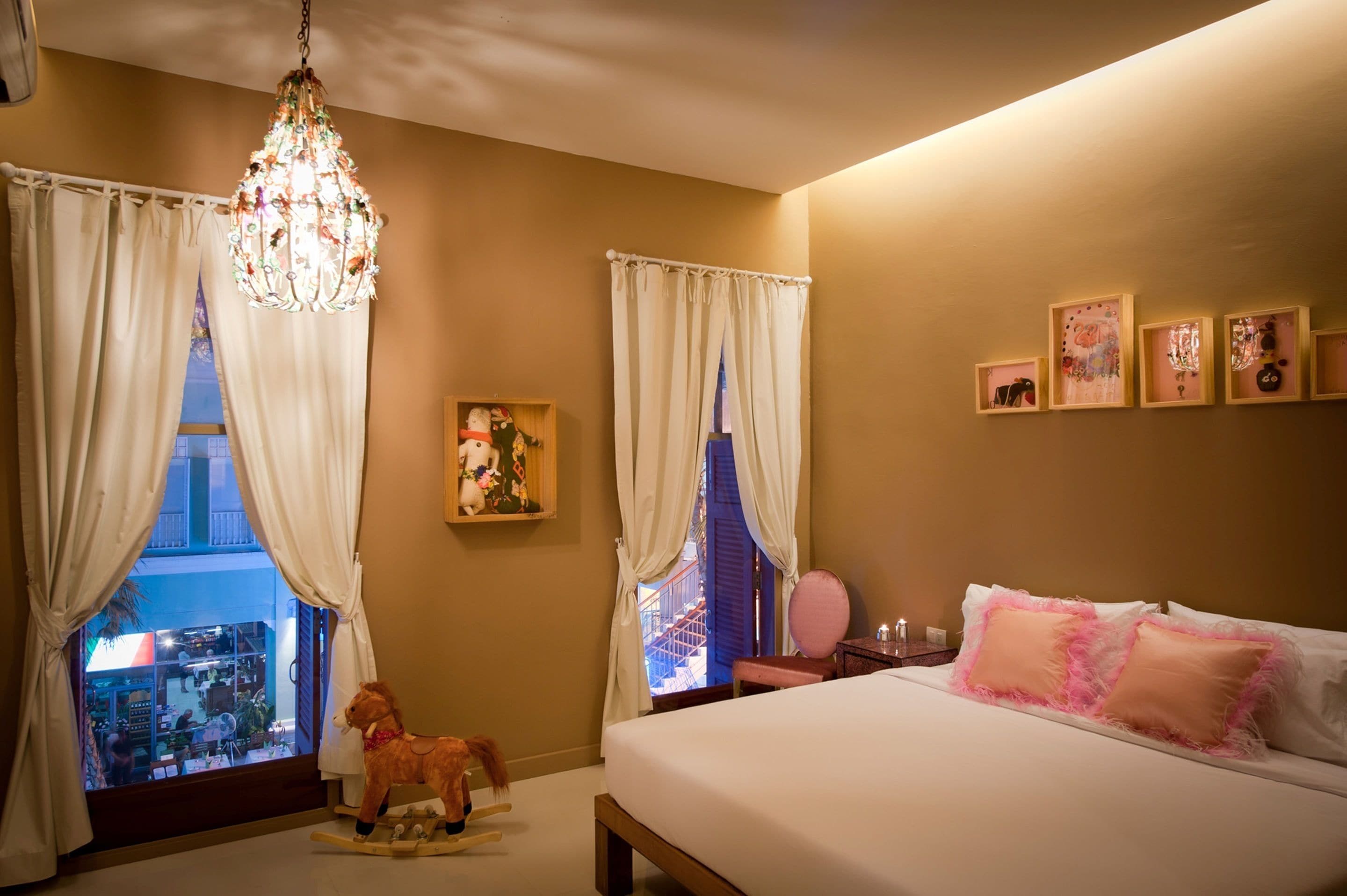 Une chambre à coucher avec un lit, un lustre, des rideaux, une fenêtre donnant sur un beau paysage et des tableaux encadrés accrochés au mur.