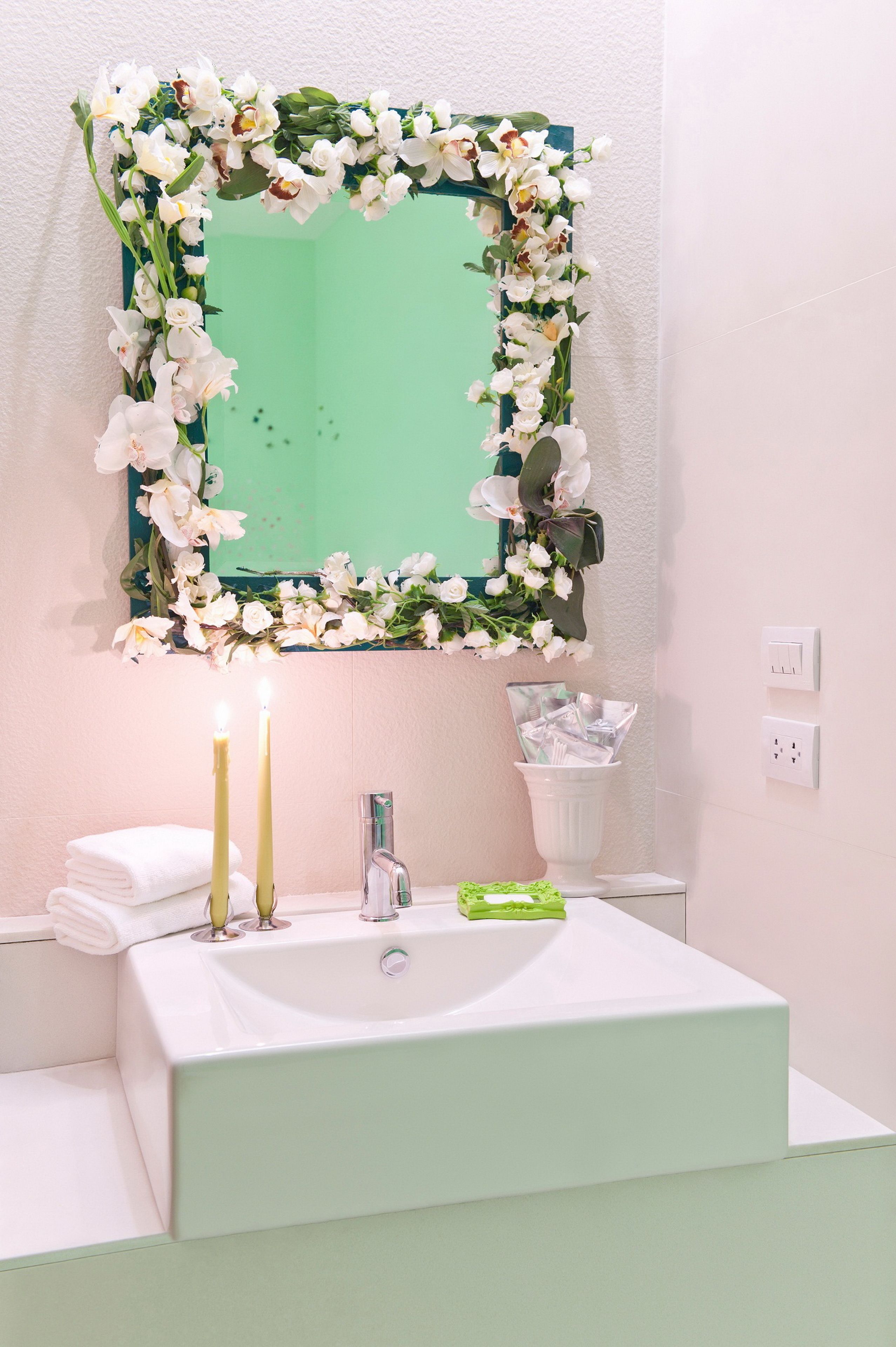 A bathroom with a white sink, two candles, and a mirror framed with white flowers.
