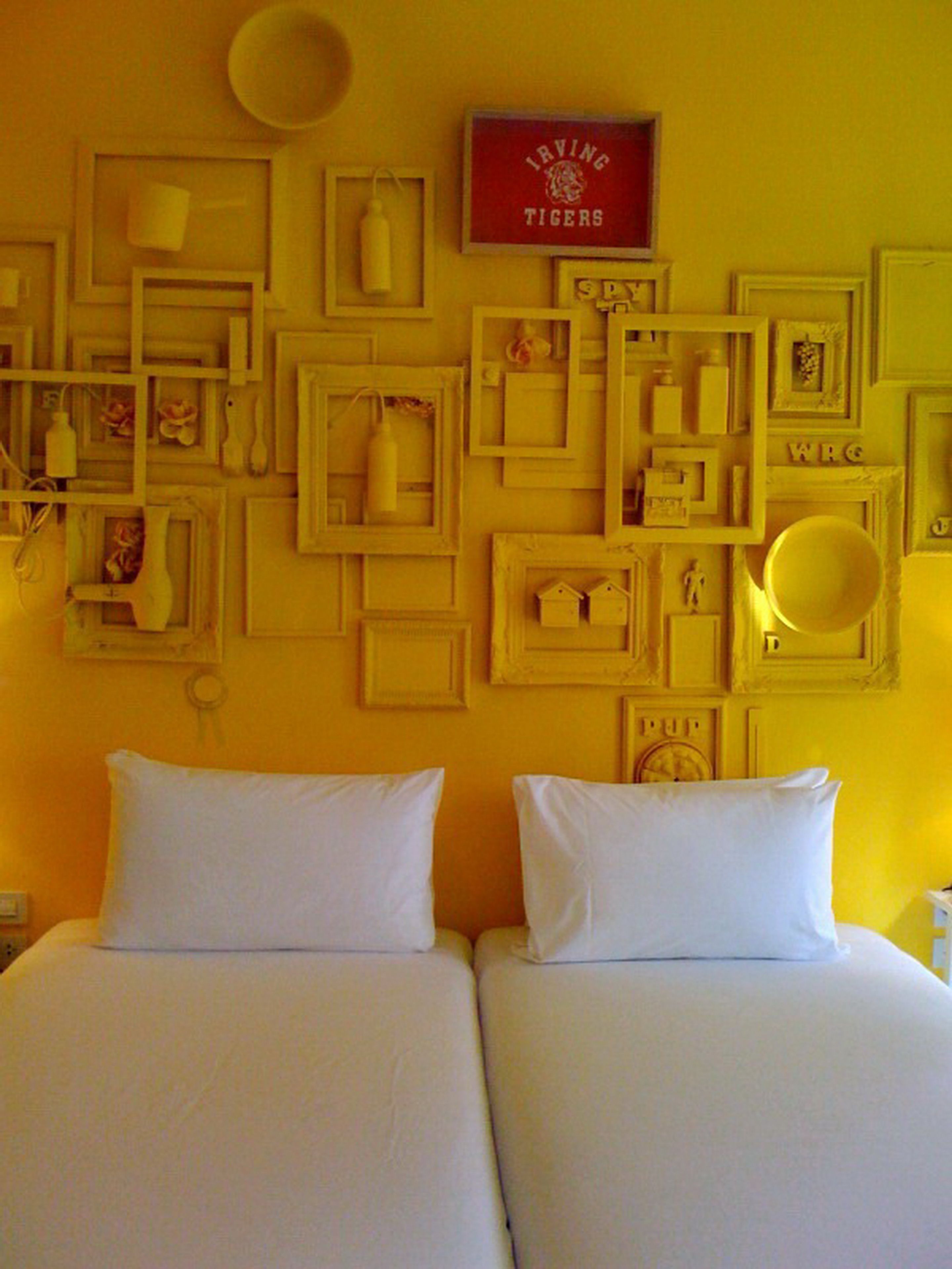 A hotel room with two beds, a wall decorated with framed pictures and mirrors, and a sign that reads "IRVING TIGERS".