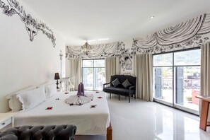 A spacious hotel room with a large bed, a black leather chair, and a view of the city through large windows. - Pimnara Boutique Hotel (Patong)