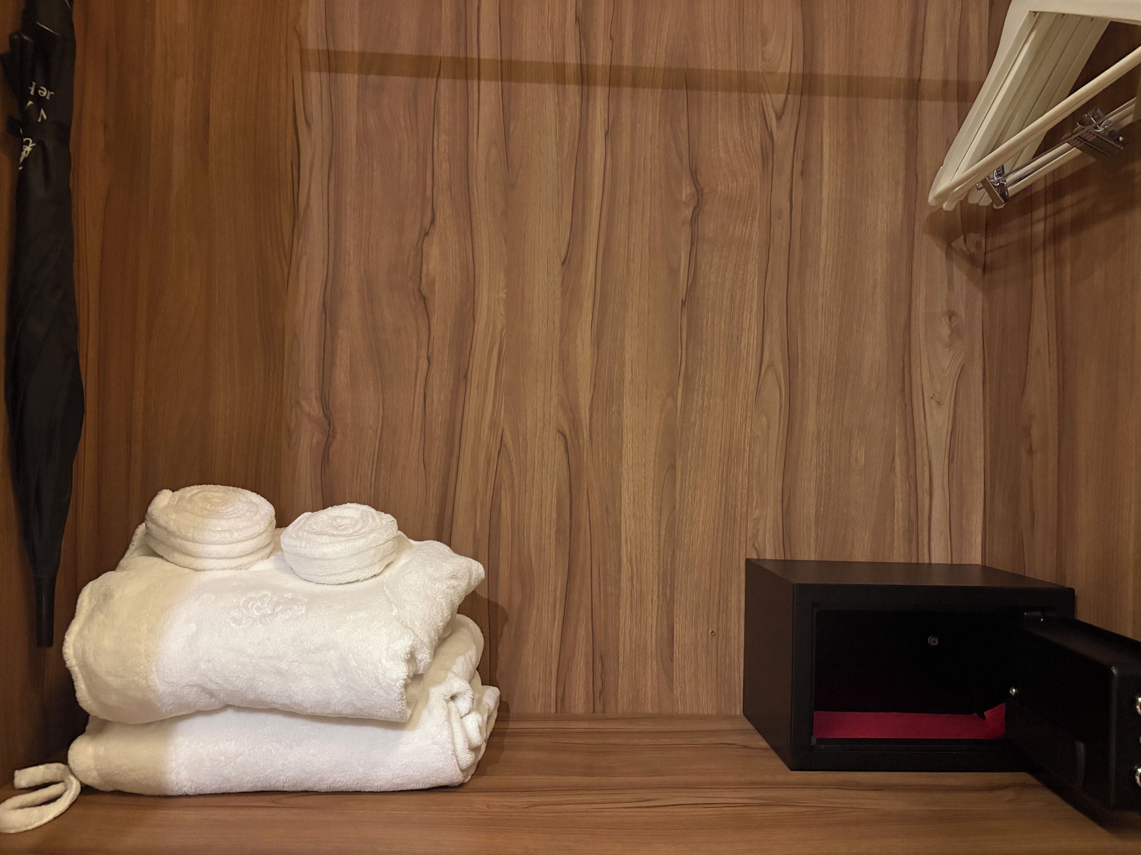 A wooden wall, a stack of white towels, and a black electronic device on a wooden surface.