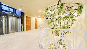 Un corridoio con ringhiera bianca, una struttura decorativa con fiori e un ascensore in vetro sulla sinistra.