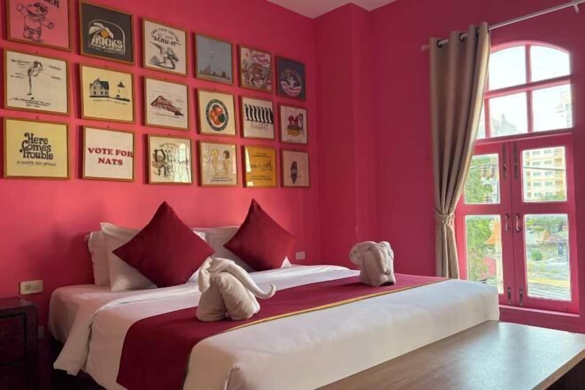 A hotel room with a red wall, a bed with red and white bedding, and a window with curtains.