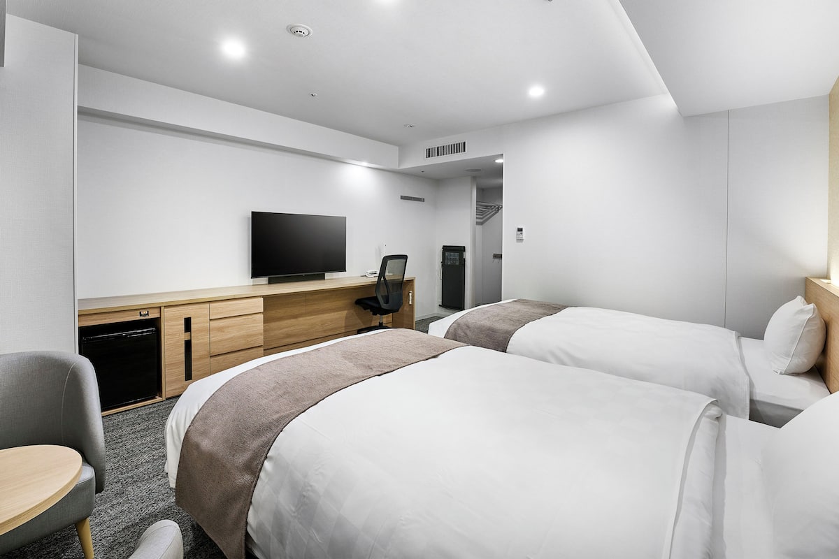 Una habitación de hotel moderna con dos camas, un escritorio con televisor de pantalla plana, una silla y una mesita.