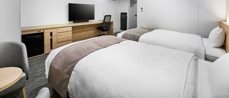 Una habitación de hotel moderna con dos camas, un escritorio con televisor de pantalla plana, una silla y una mesita.