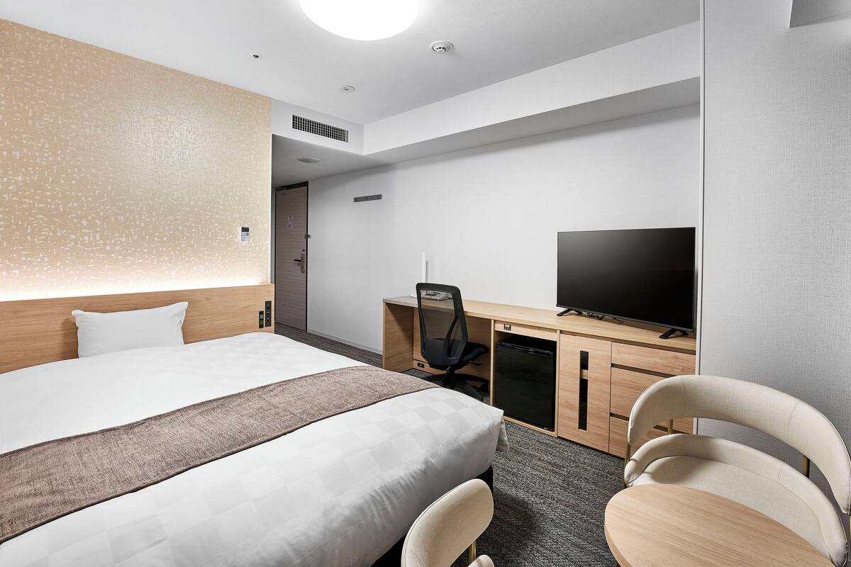 Habitación de hotel con cama, escritorio con televisor y una silla.