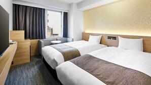 A hotel room with two beds, a desk, a chair, a small table, and a window with curtains.