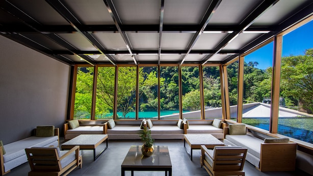 Um lounge moderno com vista para uma piscina azul-turquesa e vegetação exuberante.