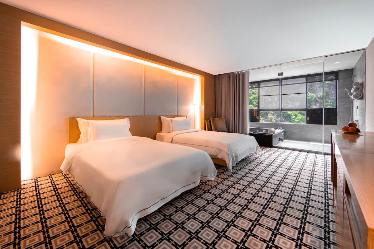 A hotel room with two beds, a patterned floor, a large window, and a balcony with a view.