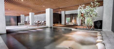 A modern spa area with a heated floor, seating area, and a wooden ceiling.
