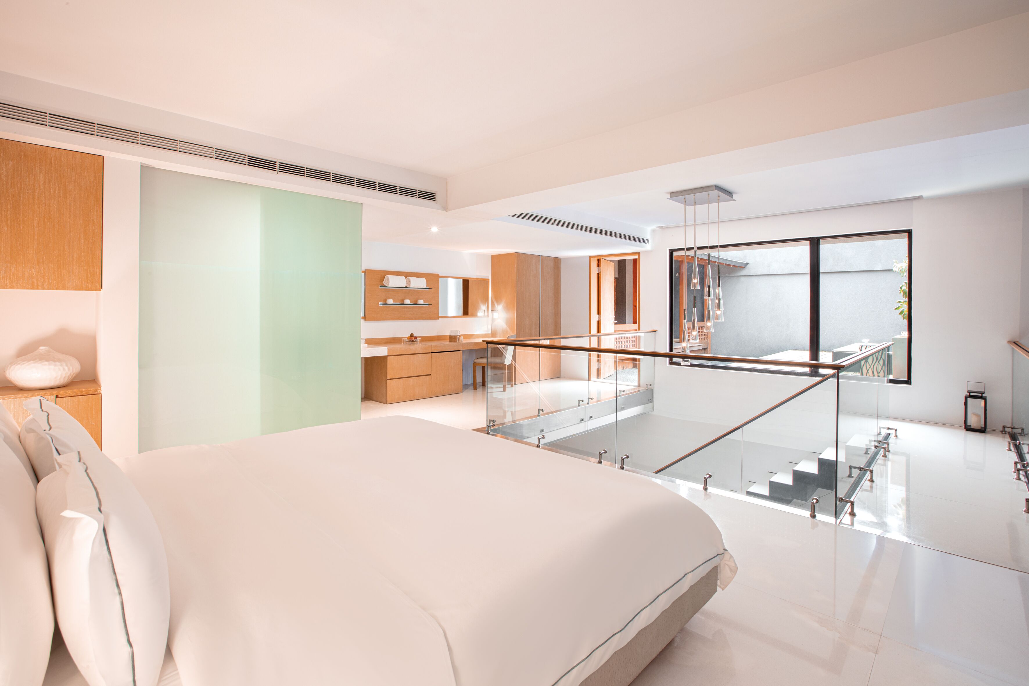 Ein modernes Hotelzimmer mit einem großen Bett, einer Glasstiege und Blick auf die Küche und den Wohnbereich.