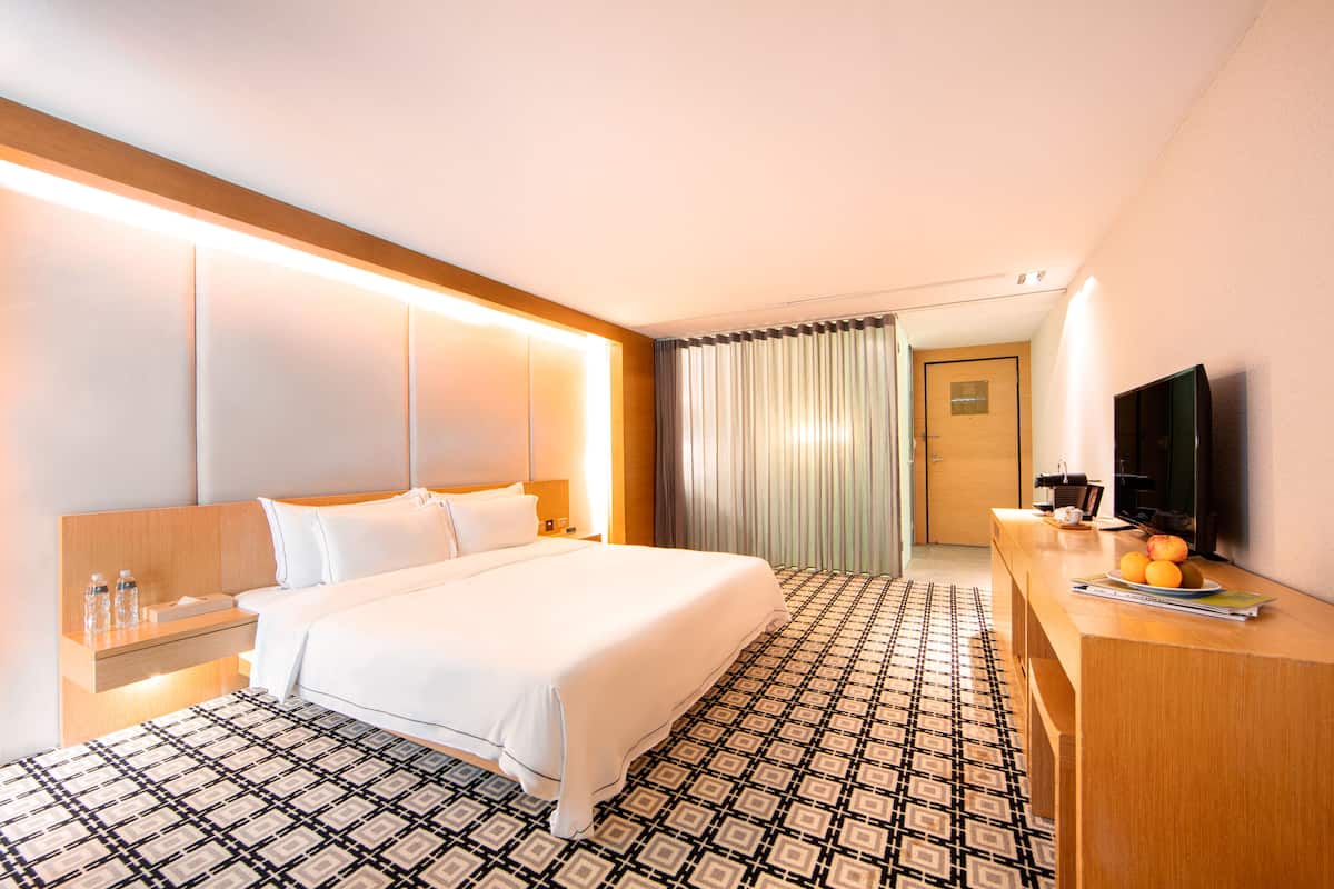 A hotel room with a large bed, bedside tables, a TV, and a patterned floor.