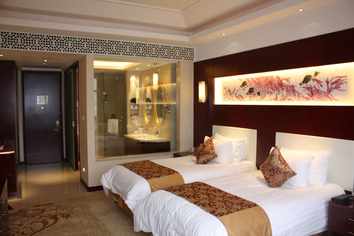 Une chambre d’hôtel avec deux lits, un grand miroir, une salle de bain avec un lavabo et une œuvre d’art accrochée au mur.