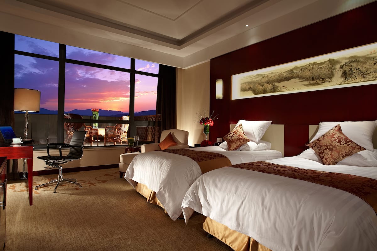 Une chambre d’hôtel avec deux lits, un bureau et une grande fenêtre donnant sur le coucher de soleil.