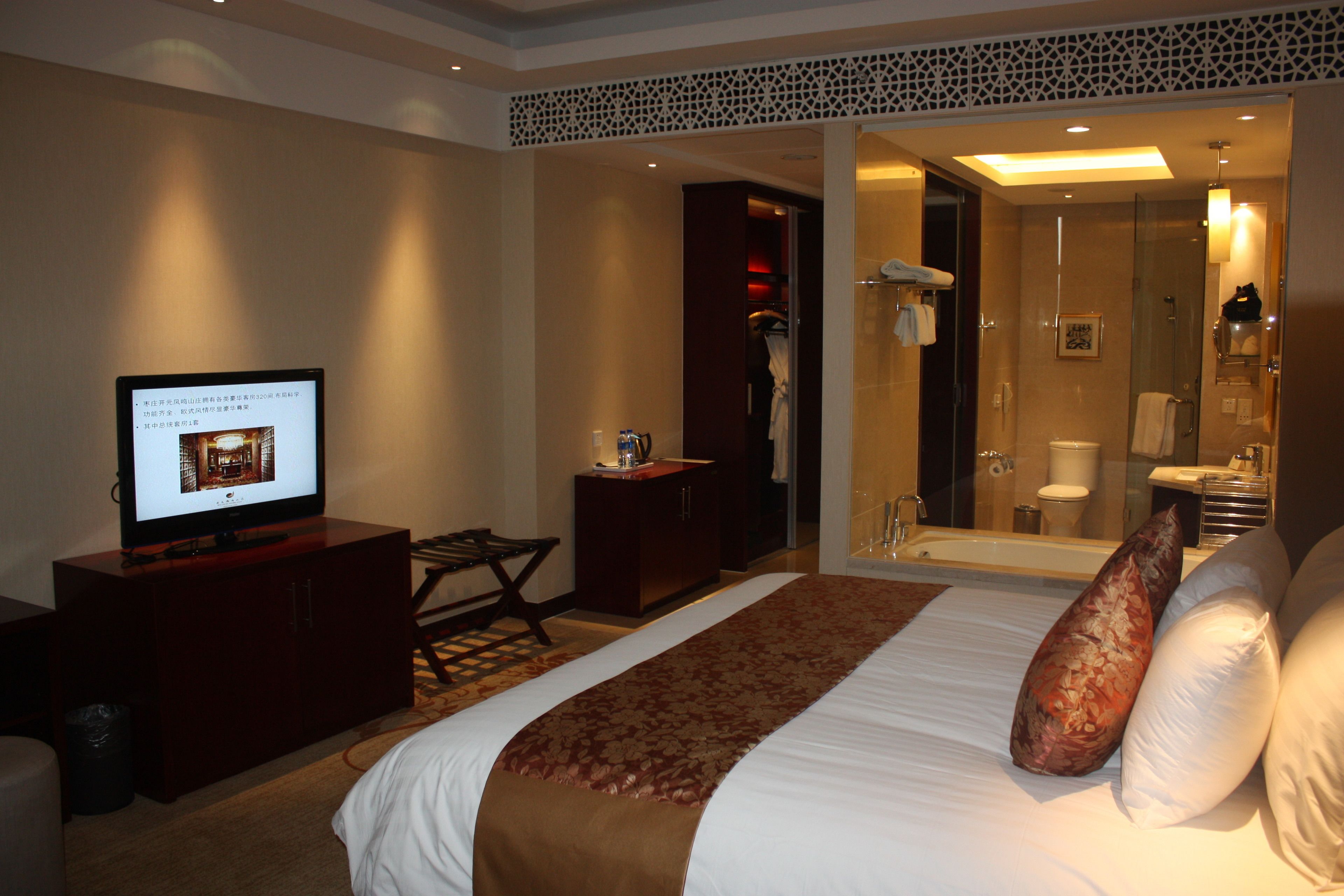 A hotel room with a bed, a television, a desk, and a bathroom visible through an open door.