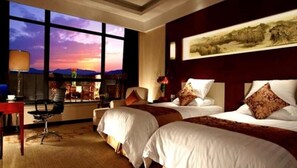 Habitación de hotel con dos camas, un escritorio y un ventanal grande con vistas al cielo.