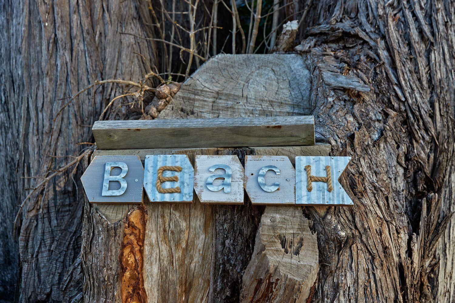 A wooden sign with the word "Beach" spelled out in metal letters attached to a tree trunk.
