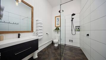Un baño moderno con un espejo grande, un tocador negro, cabina de ducha de vidrio y un inodoro blanco.