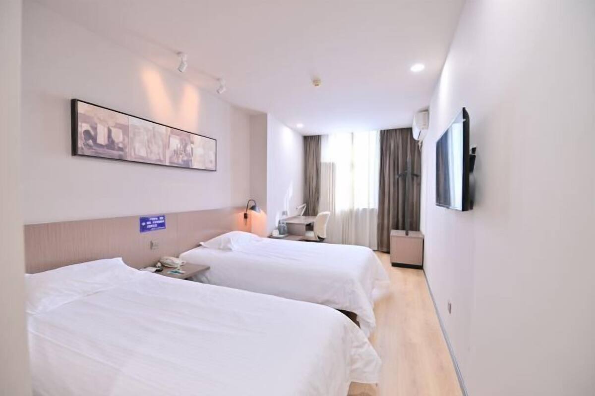 A hotel room with two beds, a desk, a chair, a TV, and a painting on the wall.
