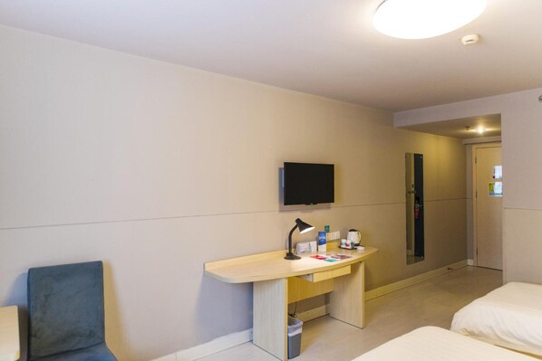 A hotel room with a bed, a desk with a chair, a television, and a door.