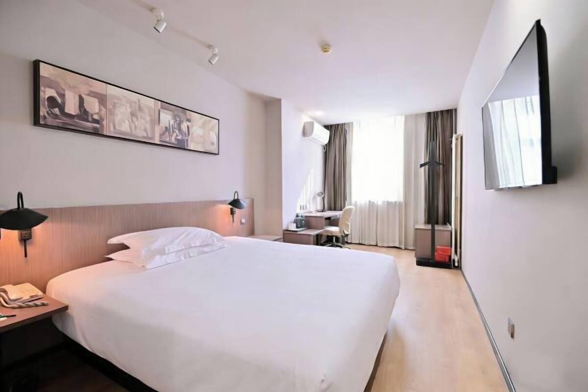 A hotel room with a large bed, a desk, a chair, a flat-screen TV, and a painting on the wall.