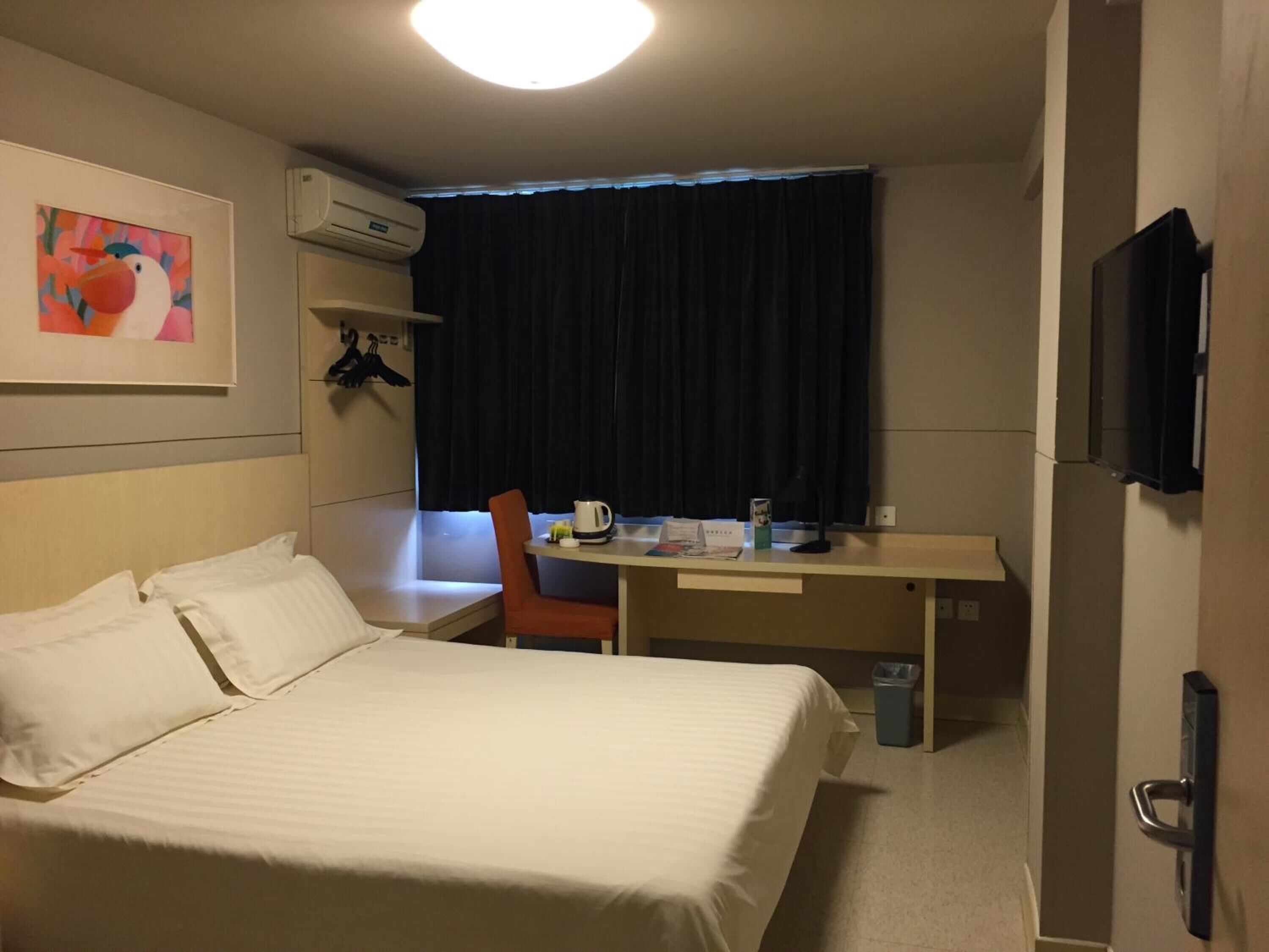 Habitación de hotel con cama, escritorio, silla, televisor y un cuadro en la pared.