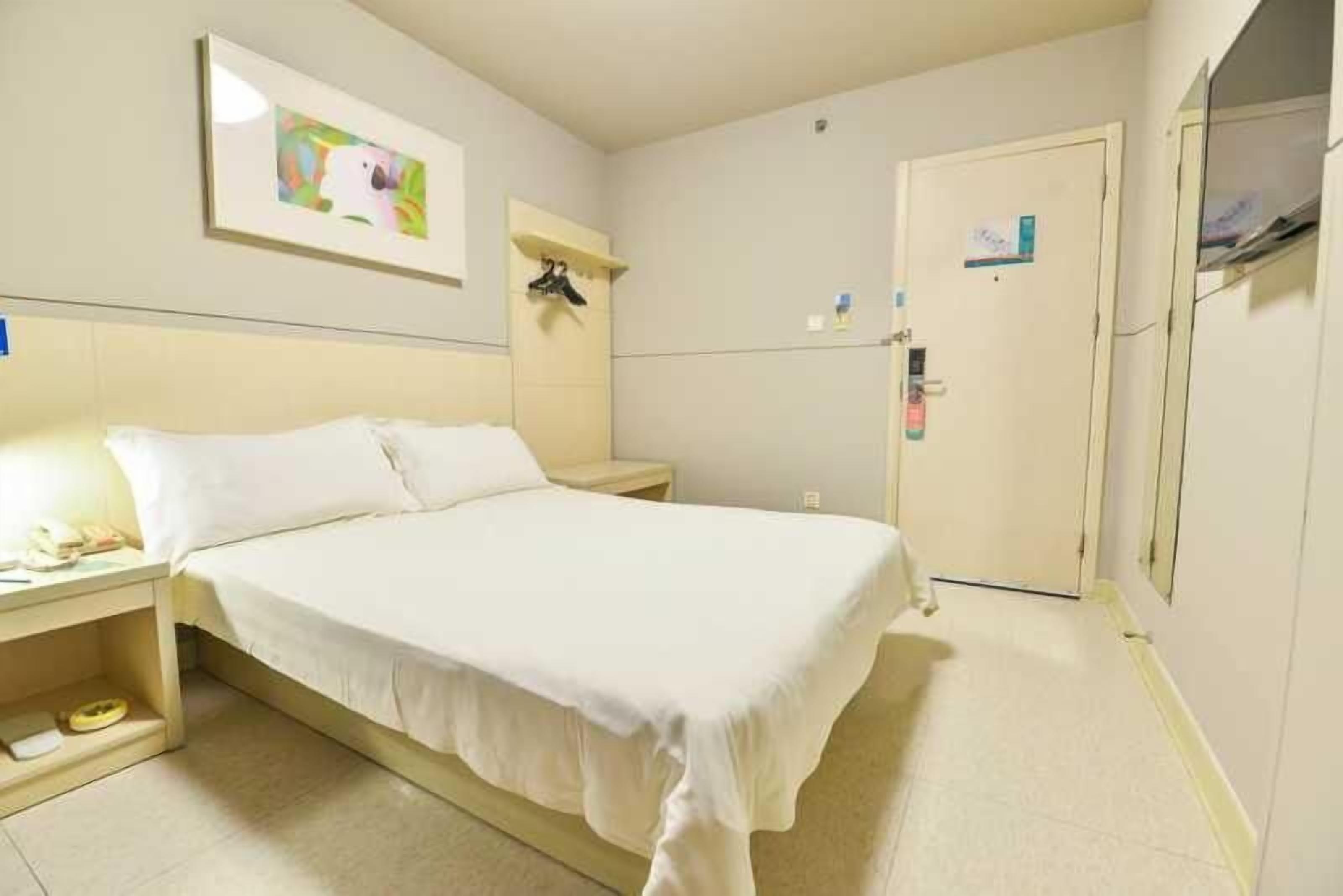 Une chambre d’hôtel avec un lit, une table de chevet et une petite étagère où sont posés des objets personnels.
