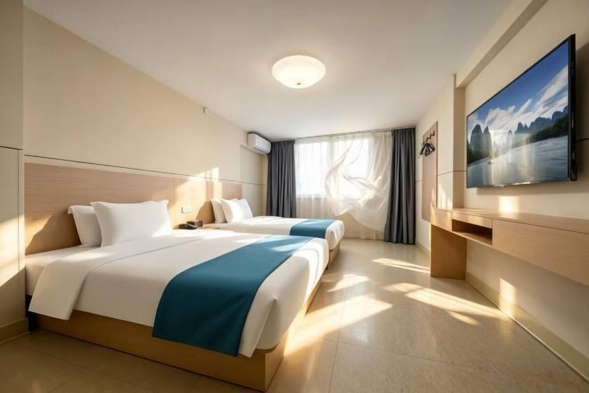 A hotel room with two beds, a flat-screen TV, a painting, and a window with curtains.