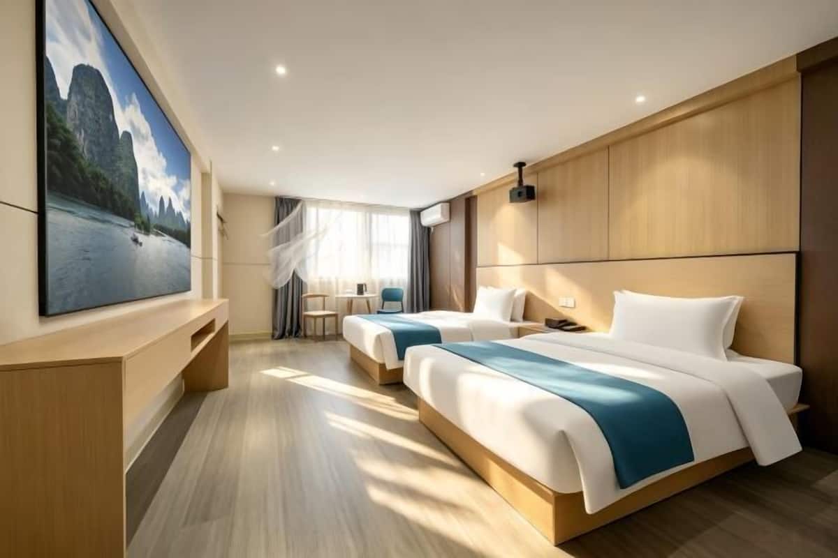 A hotel room with two beds, a large TV, a desk, and a window with curtains.