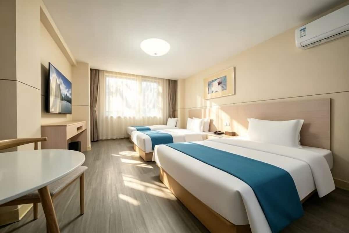 A hotel room with two beds, a desk, a chair, and a television.