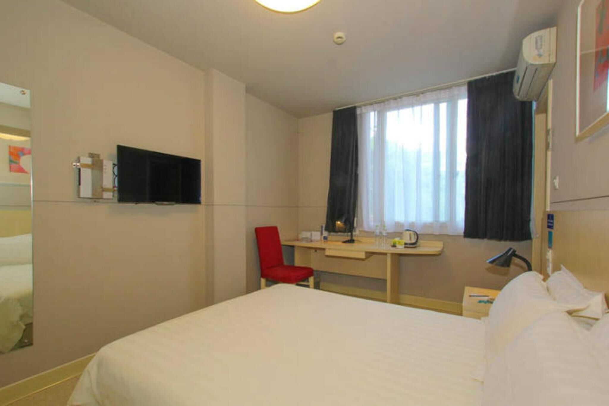 A hotel room with a bed, a desk, a chair, a TV, and a window with curtains.