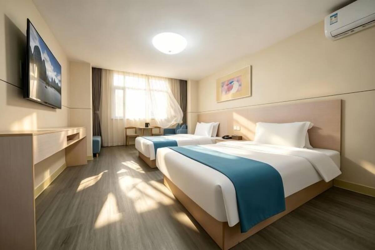 A hotel room with two beds, a desk, a chair, a TV, and a window with curtains.
