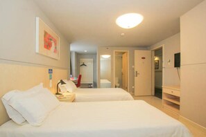 Une chambre d’hôtel avec deux lits, un bureau avec une lampe, un porte-manteau et une armoire.