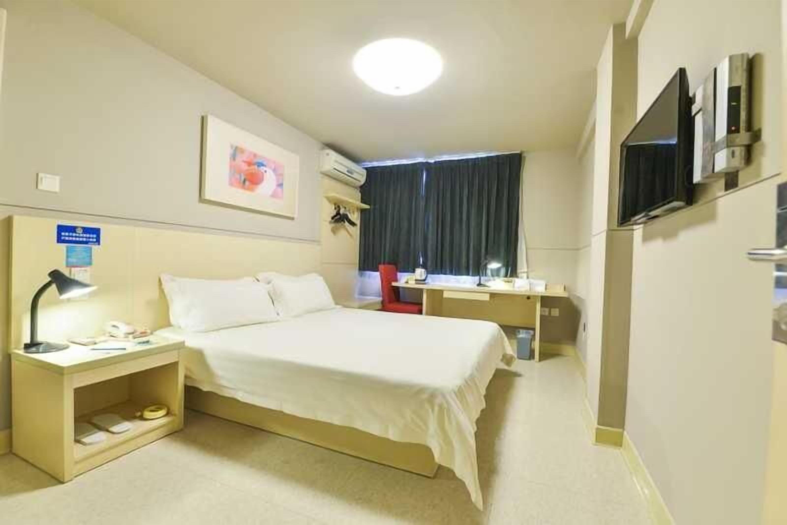 Habitación de hotel con cama, mesita de noche, lámpara, televisor y escritorio con silla.
