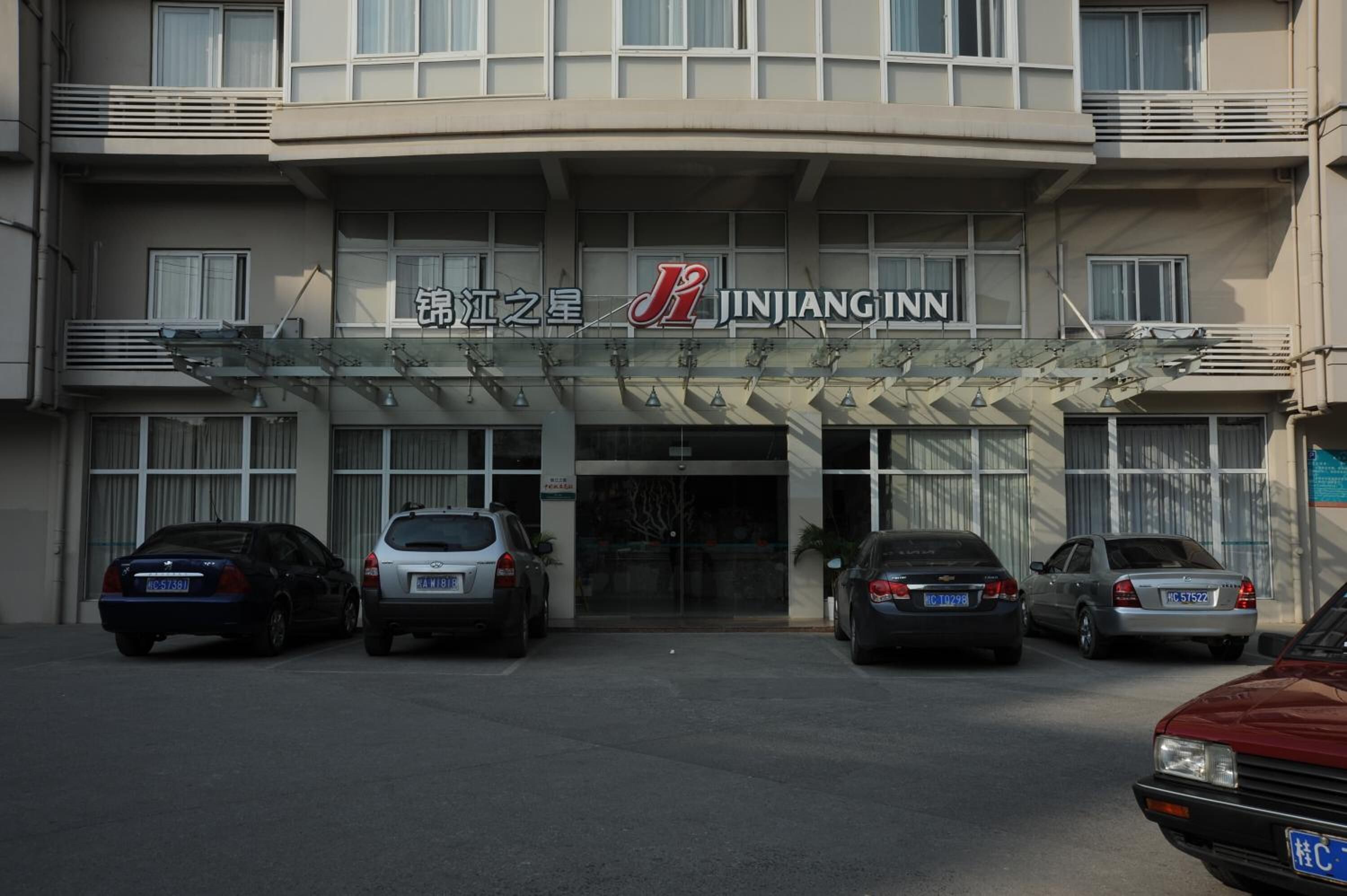 A hotel entrance with a sign reading "Jinjiang Inn" and several cars parked in front.