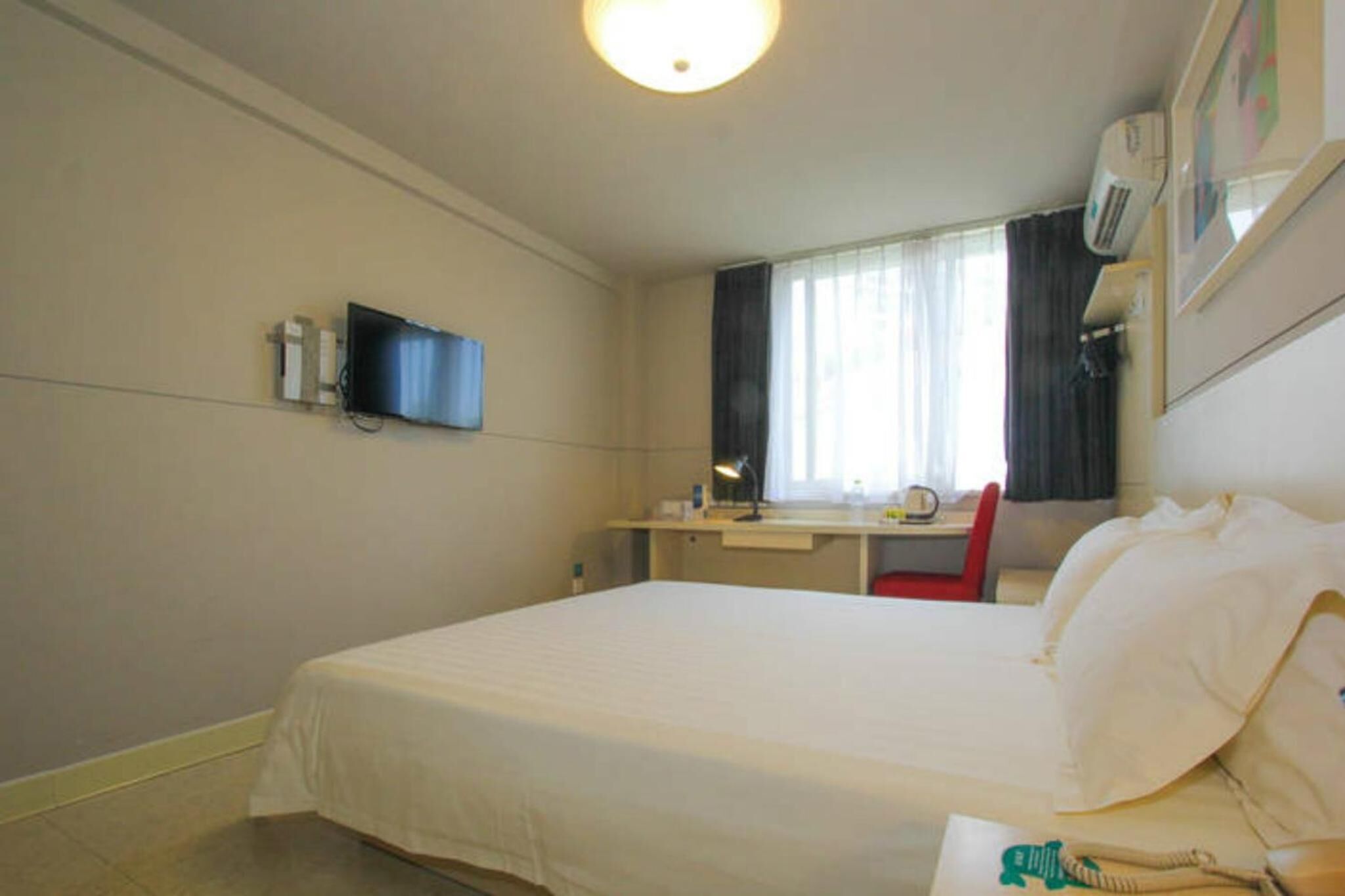 Une chambre d’hôtel équipée d’un lit, d’un bureau, d’une chaise, d’une télévision et d’une fenêtre avec des rideaux.