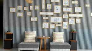 Um quarto com duas poltronas cinzentas, uma mesa redonda pequena e uma parede decorada com obras de arte emolduradas.