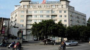 Um hotel com vários andares, fachada com sinalização marcante, varandas e vista da rua com pedestres e veículos.