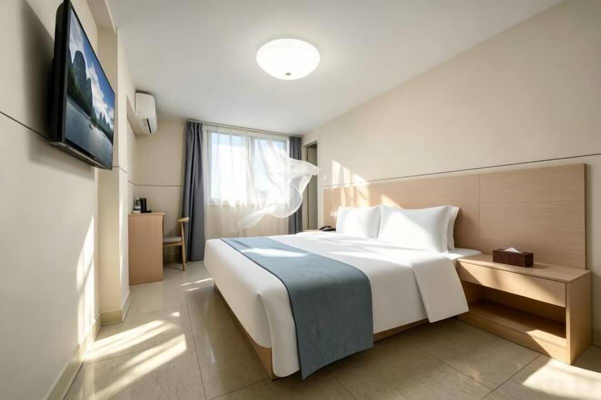 A hotel room with a bed, bedside table, TV, and a window with curtains.