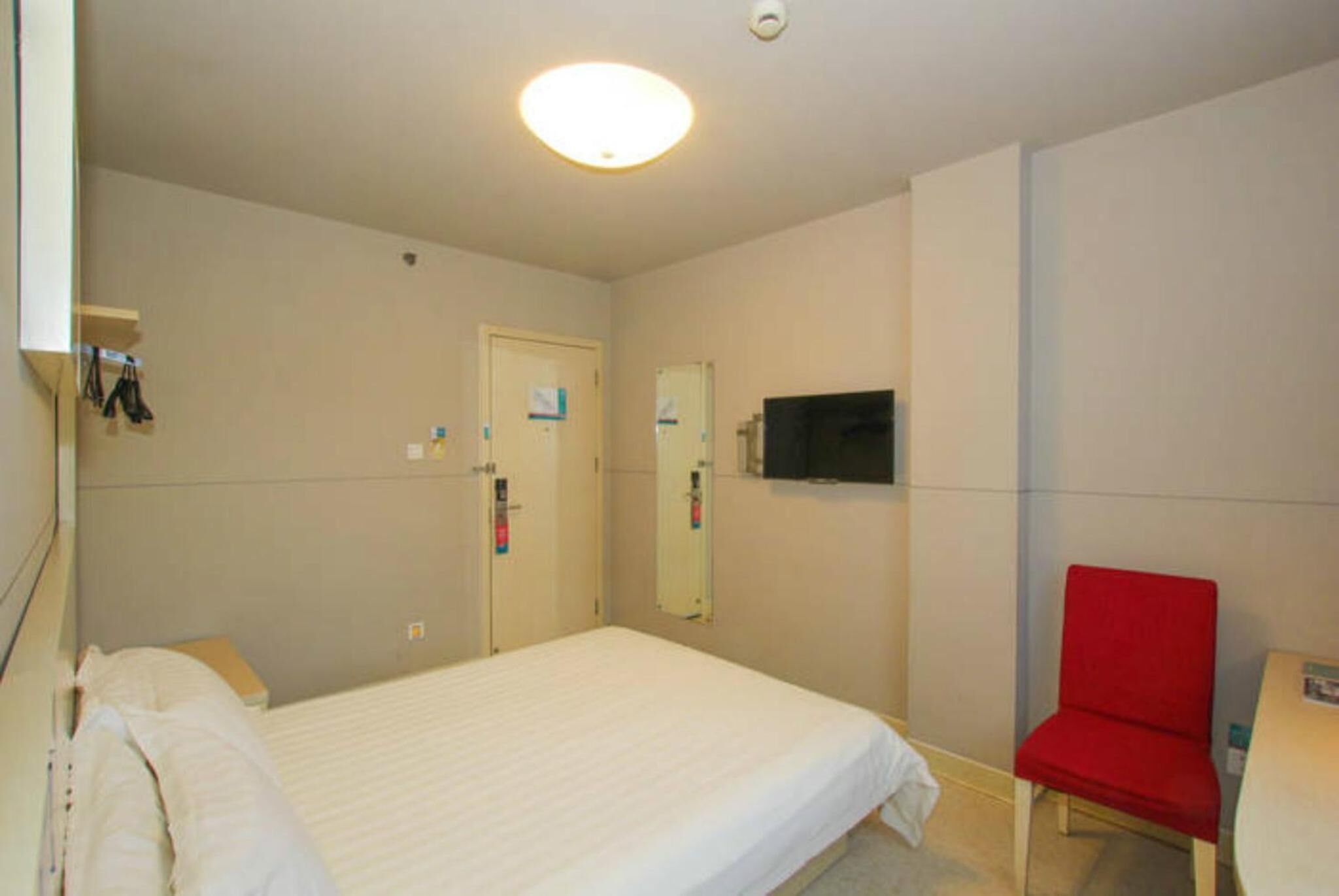 A room with a bed, a red chair, a television, and a door with a mirror.