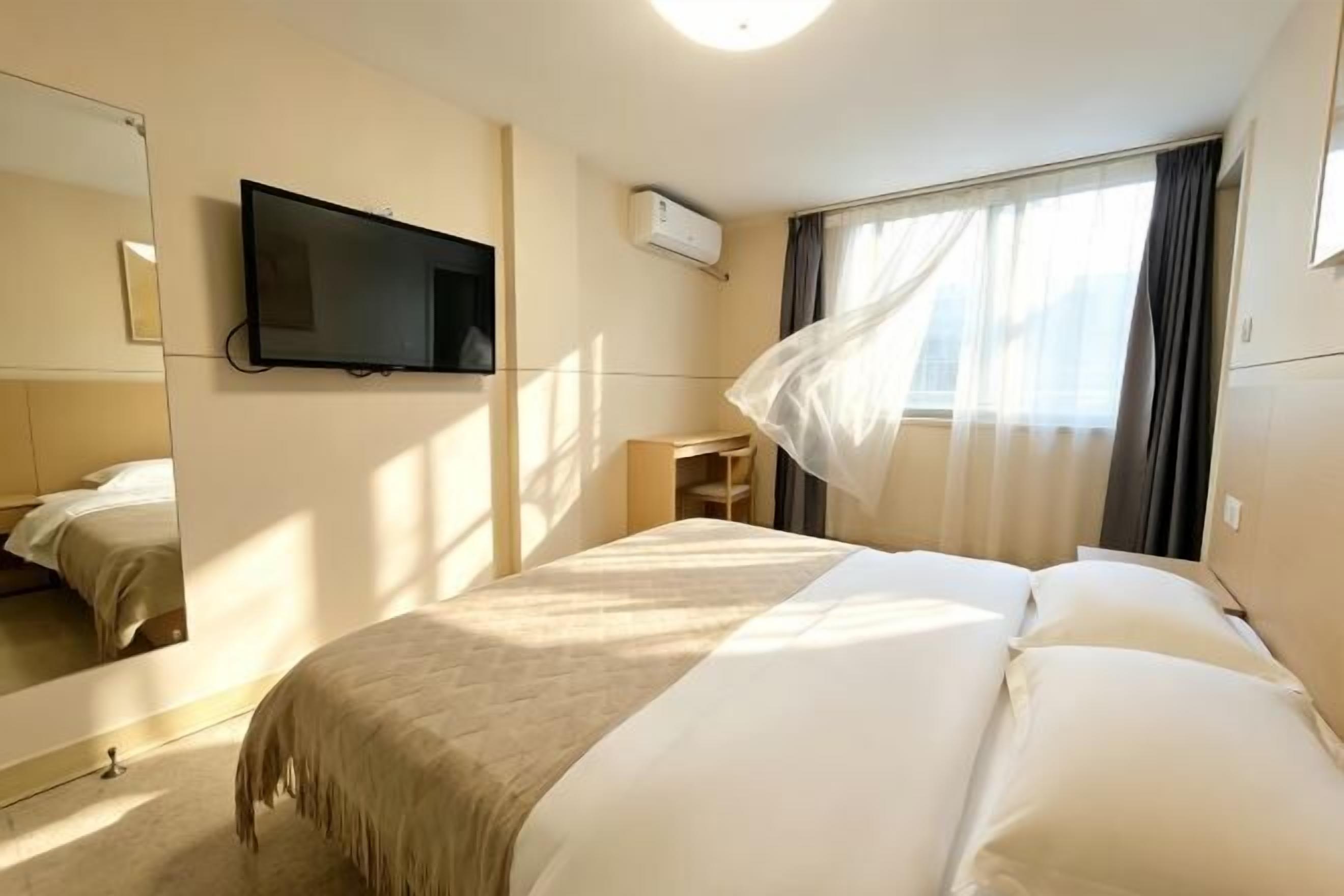 A hotel room with a bed, a TV, a desk, and a window with curtains.