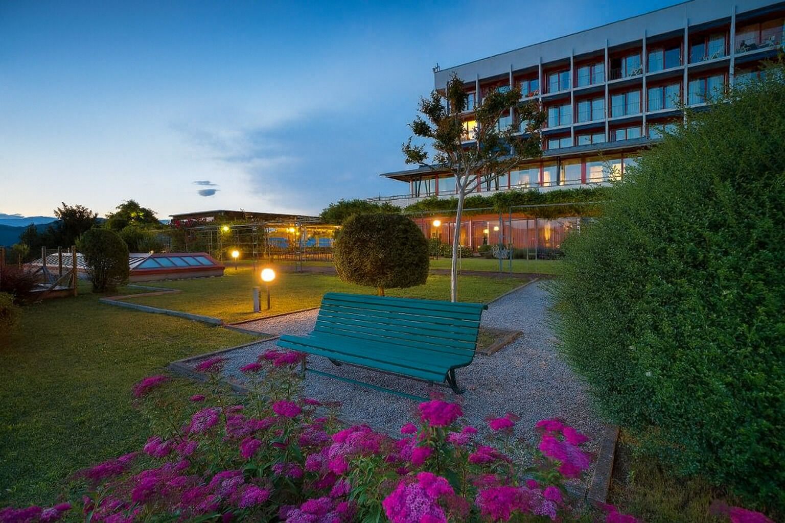 A modern building with a green bench and purple flowers in the foreground.