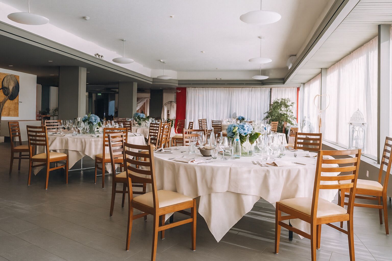 A spacious dining area with round tables, wooden chairs, and white tablecloths.