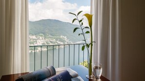 Un balcon avec vue sur un lac et des montagnes, un verre d’eau et une serviette enroulée.
