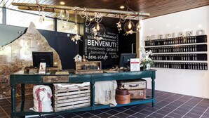 Un comptoir de café au design rustique, avec un mur en pierre, des étagères en bois où sont exposées des bouteilles de café et un tableau noir sur lequel est écrit le mot « BENVENUTI ».