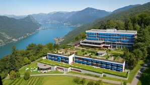 Un ensemble immobilier moderne composé de plusieurs bâtiments aux façades bleues et blanches, entouré d’une végétation luxuriante et bordé d’un lac.