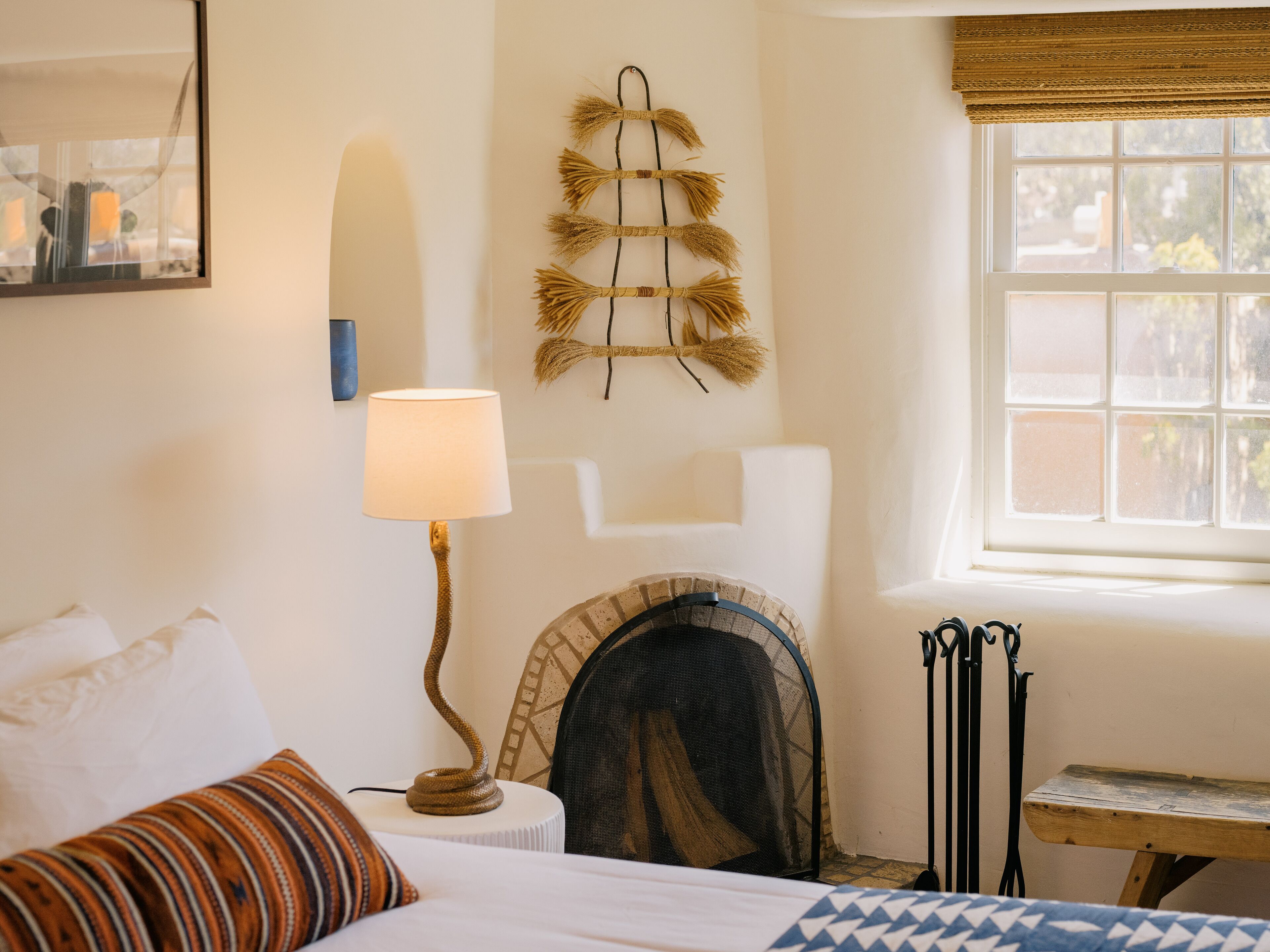 Un dormitorio con cama, lámpara, chimenea, ventana y un adorno en la pared.
