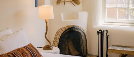 Un dormitorio con cama, lámpara, chimenea, ventana y un adorno en la pared.